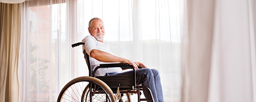 Photo of a man in a wheelchair sitting in front of large windows.